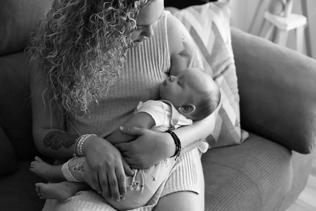Fotografía documental de lactancia a domicilio en Barcelona: Madre amamantando a su bebé en sofá, blanco y negro.