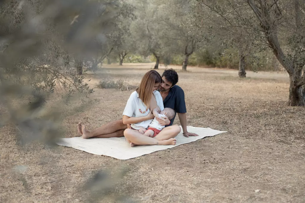 Fotografía de familia en exterior en Barcelona: Padres y bebé recostados en el campo, tranquilidad.