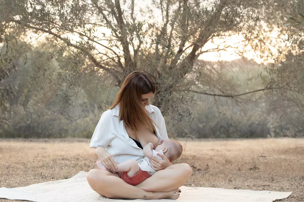 Fotografía de bebés en exterior en Barcelona: Madre sentada en el campo con su bebé.