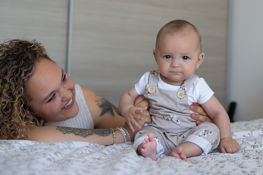 Fotografía de bebés en Barcelona: Bebé sonriendo en brazos de su madre, alegría.