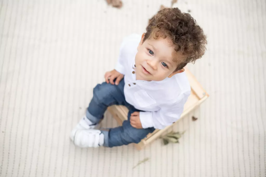 Niño pequeño con camisa blanca sonriendo desde una silla de madera durante una sesión infantil