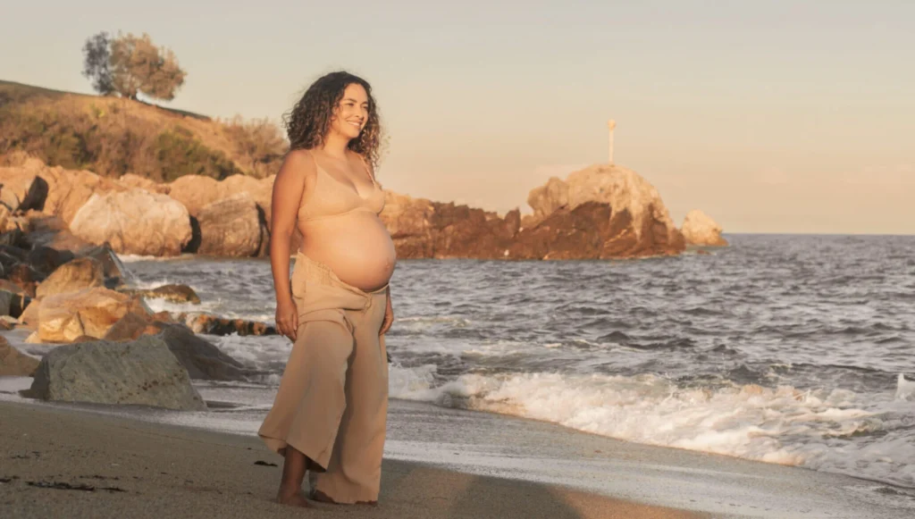 Mujer embarazada sonriendo en la playa al atardecer