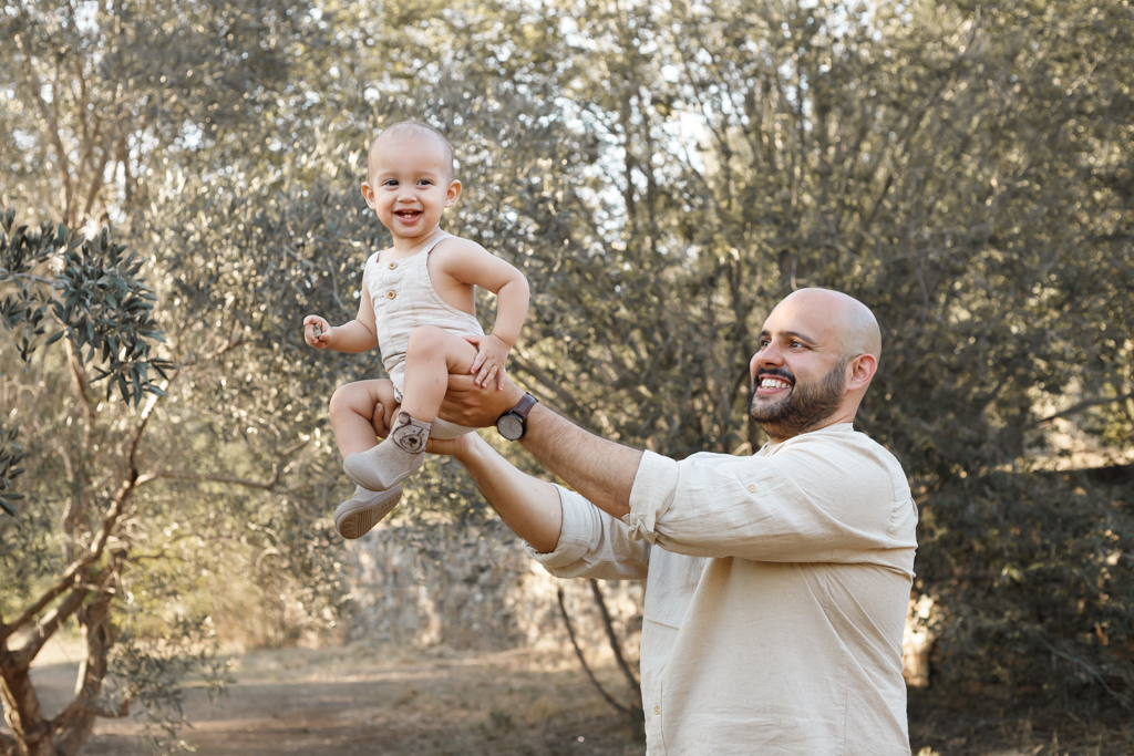 Padre levantando a su bebé en el aire en medio de árboles en Barcelona.