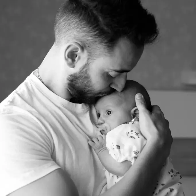Fotografía de familia en blanco y negro en Barcelona: Padre besando a su bebé, ternura.