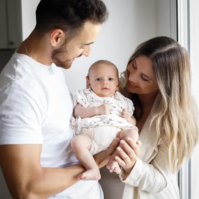 Fotografía de familia feliz en su domicilio: Padres y bebé sonriendo, alegría.