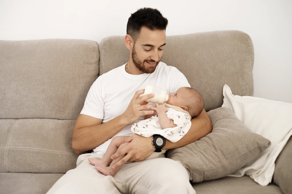Fotografía de bebés a domicilio en Barcelona: Padre con bebé en sofá, naturalidad.