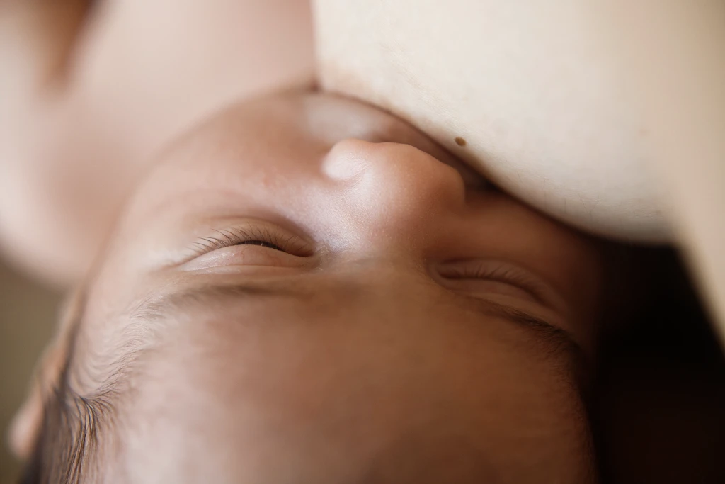 Retrato en primer plano de la cara de un bebé recién nacido tomando el pecho, capturando la serenidad de sus primeros días en Barcelona.