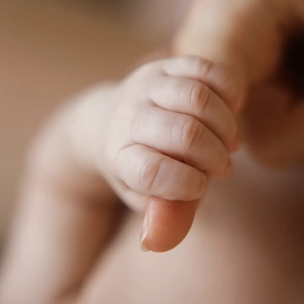 Pequeña mano de un bebé recién nacido agarrando con fuerza el dedo de su madre. Fotografía de detalles en Barcelona.