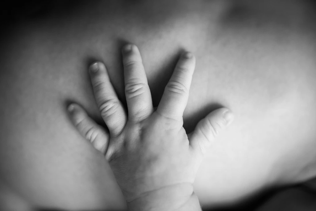 Artística fotografía en blanco y negro de la mano de un bebé recién nacido sobre el pecho de su madre, en una sesión en Barcelona.
