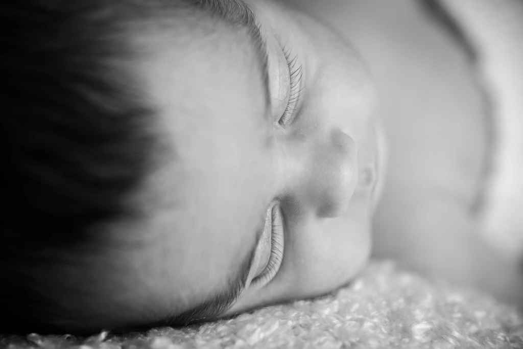 Precioso primer plano en blanco y negro de un bebé recién nacido sonriendo mientras duerme. Fotografía de detalles en Barcelona.