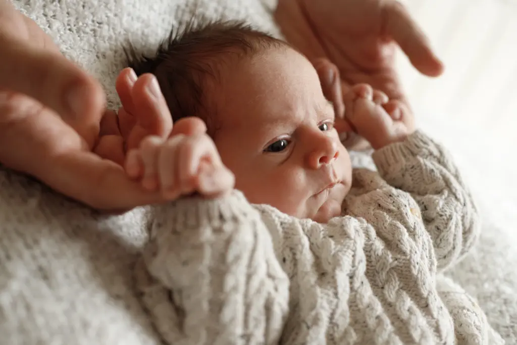 Retrato tierno de un bebé recién nacido en Barcelona, acunado por las manos de sus padres en una sesión de fotos profesional.