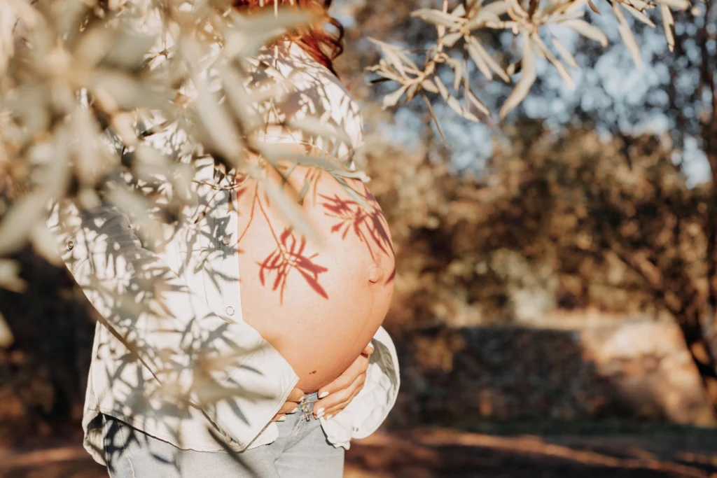 Detalle artístico de embarazo entre naturaleza en Barcelona Barriga de embarazo entre hojas de olivo en sesión de fotos natural al atardecer