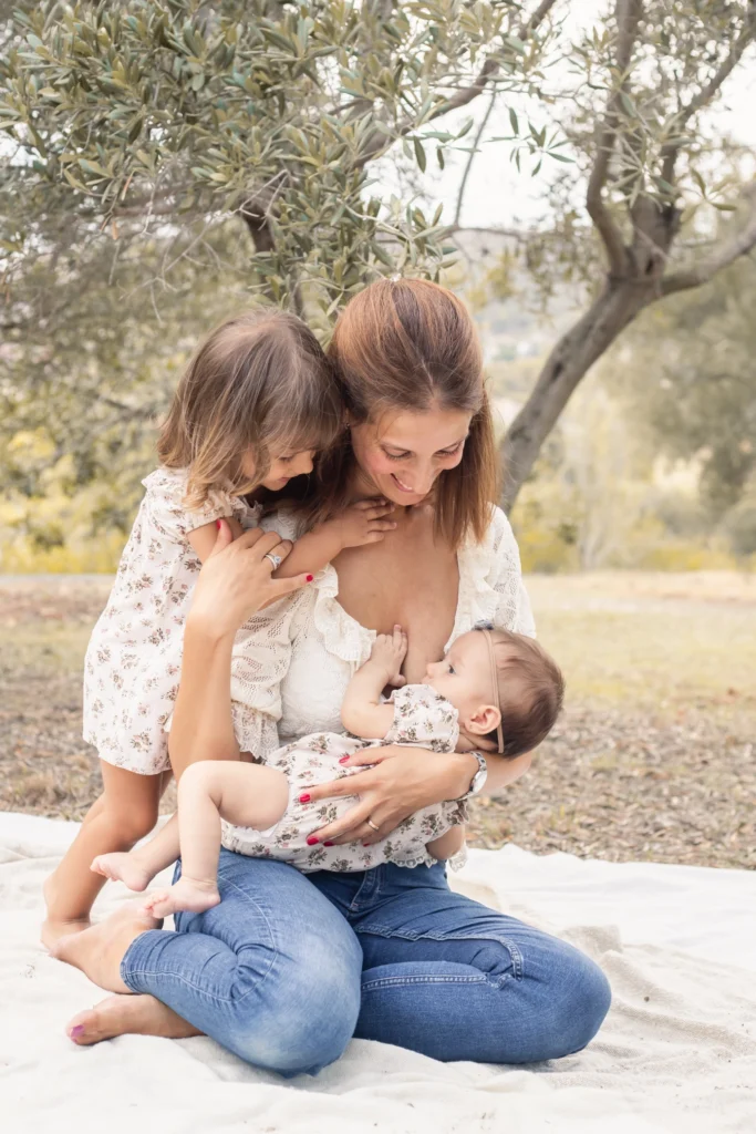 Madre con sus dos hijas pequeñas en una tierna sesión fotográfica por el Día de la Madre en Barcelona, una de ellas lactando al aire libre