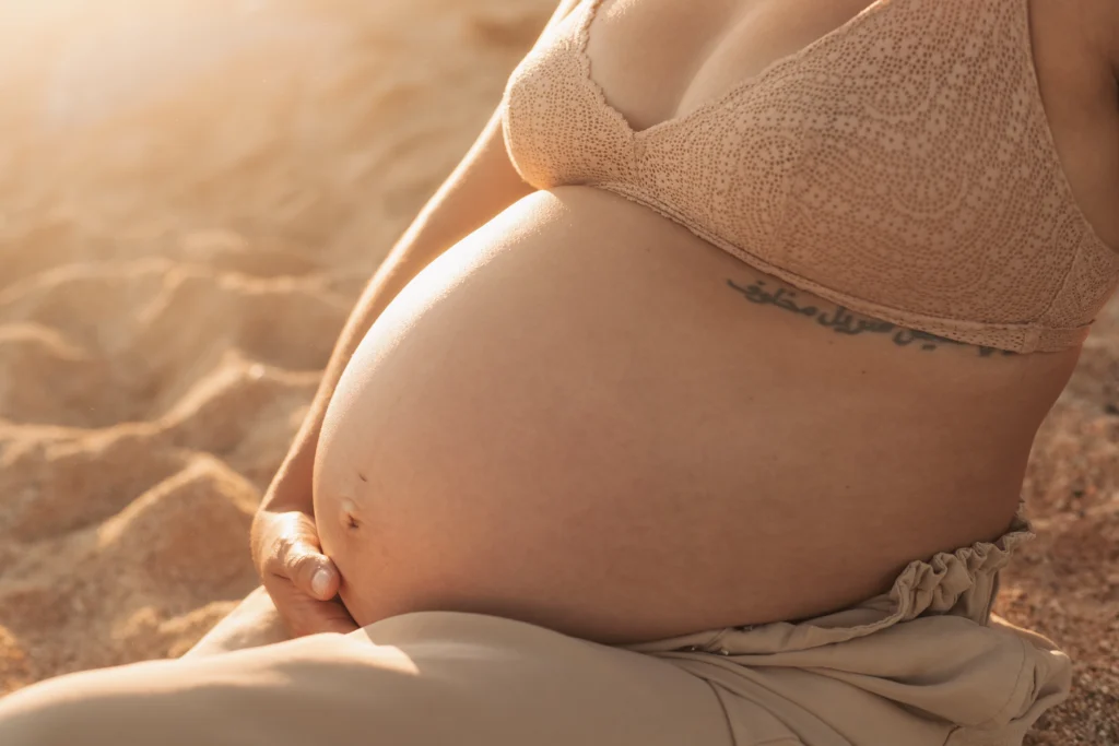 Detalle artístico de barriga de embarazada: fotografía de maternidad íntima en Barcelona. Primer plano artístico de barriga de embarazada en la playa al atardecer en un reportaje fotográfico.