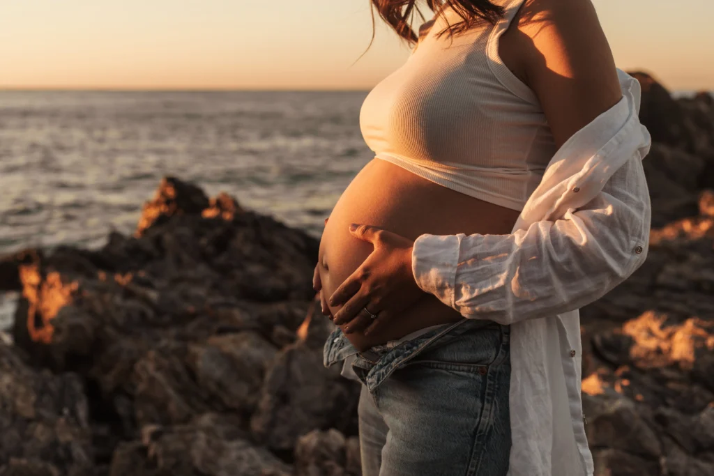 Sesión de embarazo natural en la playa con luz dorada. Mujer embarazada en una sesión de fotos al atardecer y con el mar de fondo en Barcelona
