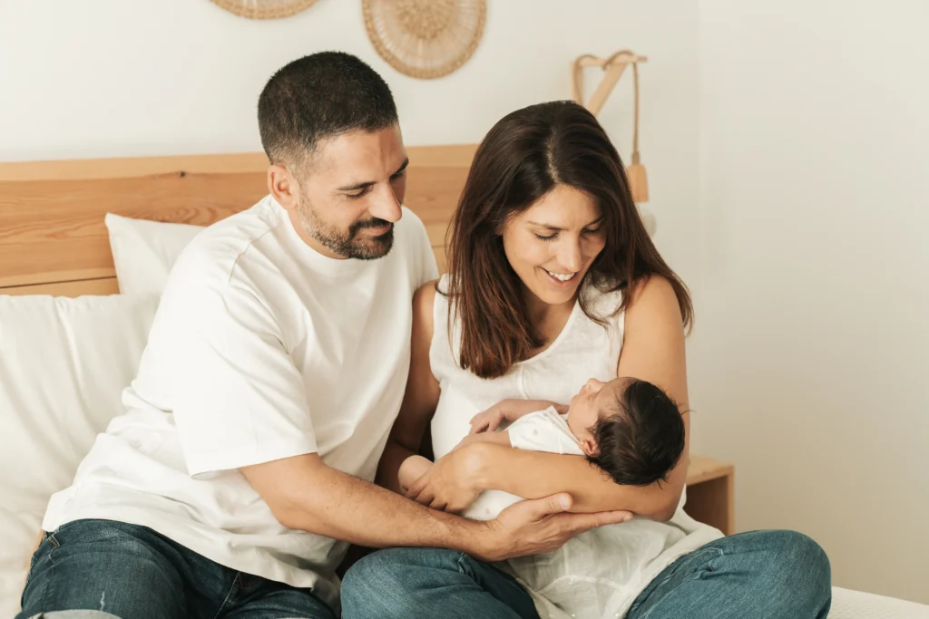 Padres abrazando a su bebé recién nacido sentados en la cama