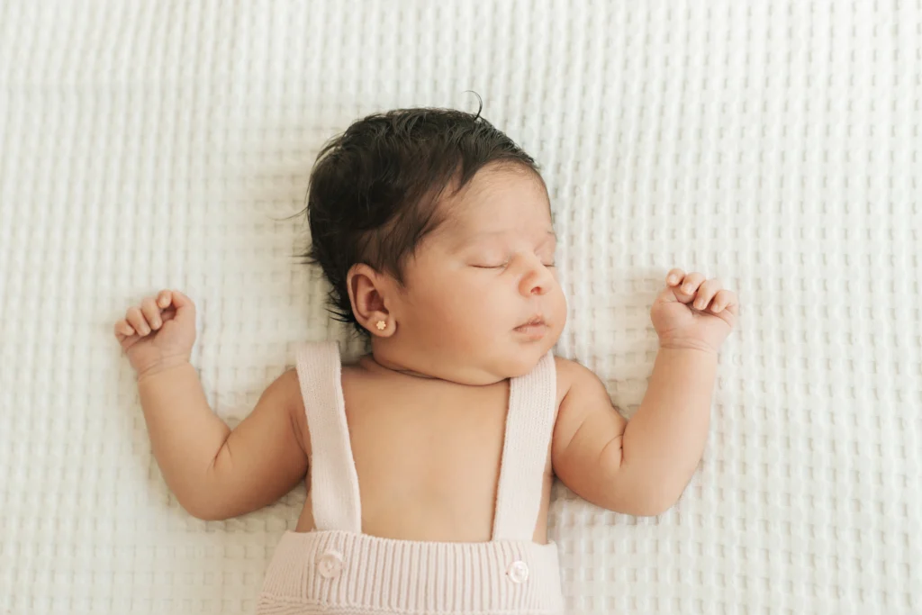 Recién nacido dormido con tirantes rosados sobre colcha blanca