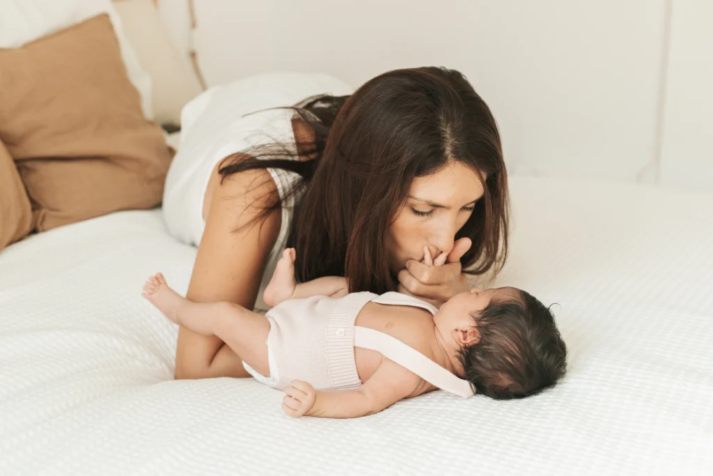 Madre besando a su recién nacido sobre la cama durante sesión en Barcelona