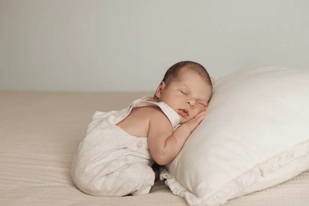Bebé dormido en posición fetal sobre superficie clara durante sesión en casa