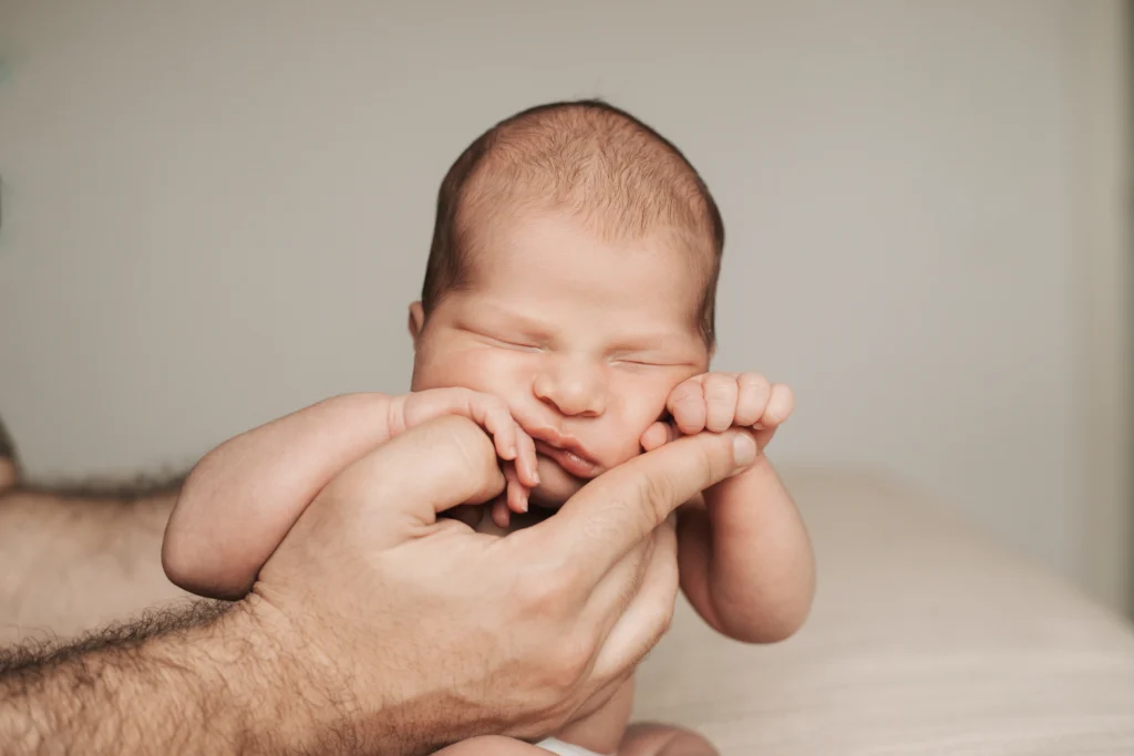 Recién nacido con los ojos cerrados sostenido por manos de su padre