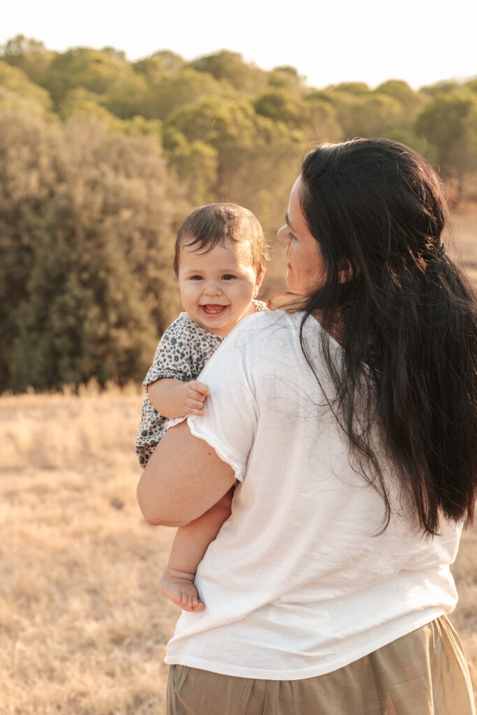 Madre sosteniendo a su bebé y contemplando el paisaje en una sesión del Día de la Madre en exteriores cerca de Barcelona