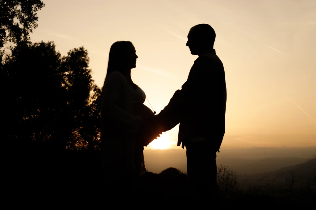Silueta artística de pareja embarazada al atardecer: reportaje de maternidad dramático y emotivo. Silueta de pareja embarazada en la montaña de Barcelona al atardecer: reportaje de maternidad familiar natural y espontáneo.