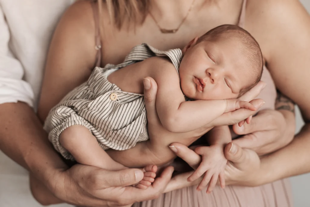 Fotografía con bebé recién nacido sostenido con delicadeza por las manos de sus padres.
