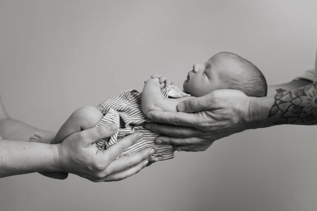 Fotografía de recién nacido en Barcelona. Detalle artístico de las manos de los padres sosteniendo al bebé en blanco y negro.