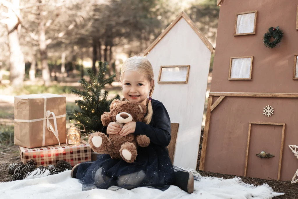 Primer plano de un niña pequeña sonriendo durante su reportaje de Navidad en el bosque con ambiente cálido.
