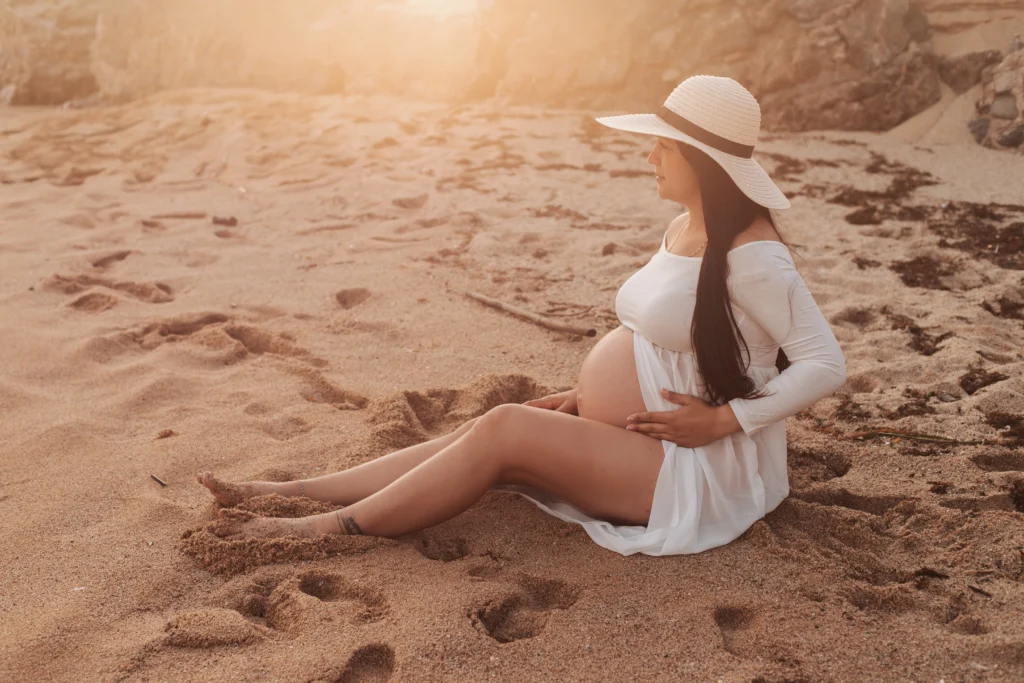 Sesión de maternidad con estilo natural: vestido blanco y sombrero en la playa de Barcelona. Sesión de maternidad natural y elegante en la playa con vestido blanco
