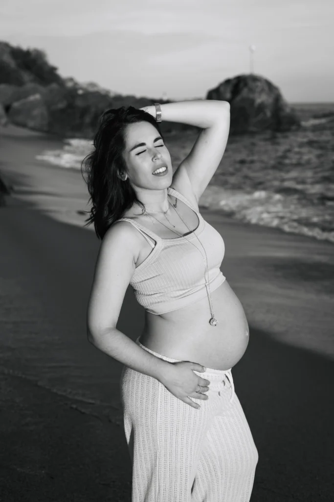 Retrato artístico de embarazada en blanco y negro en la playa: fotografía de maternidad por Saray Ruiz. Retrato artístico en blanco y negro de mujer embarazada posando en la playa al atardecer