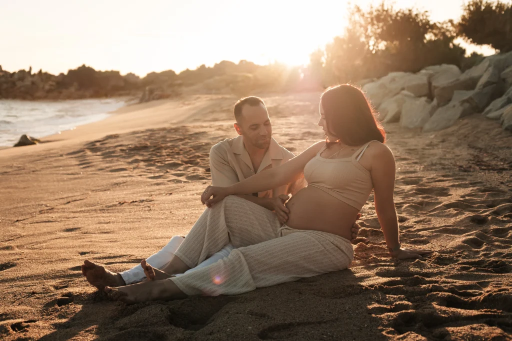 Fotos de embarazo en pareja: capturando la conexión y el amor en la playa al atardecer. Pareja posando en sesión de fotos de embarazo en la playa al atardecer