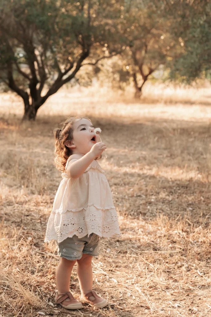 Fotografía infantil natural en Barcelona: niña pequeña soplando un diente de león en la montaña.