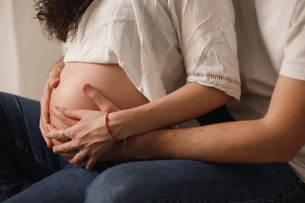 Detalle de manos en barriga de embarazada: fotografía íntima de maternidad en estudio Barcelona. Pareja acariciando la barriga de embarazo en estudio de fotos Barcelona.