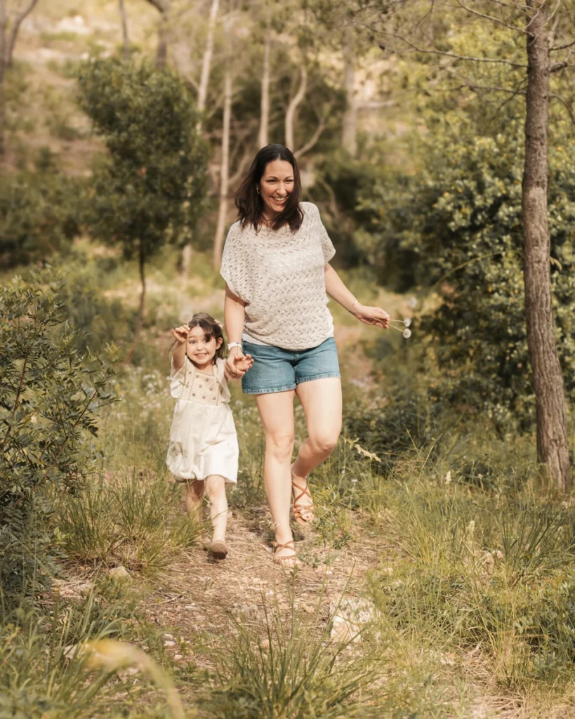 Sesión de fotos familiar en el campo de Barcelona: madre e hija sonrientes caminando de la mano.
