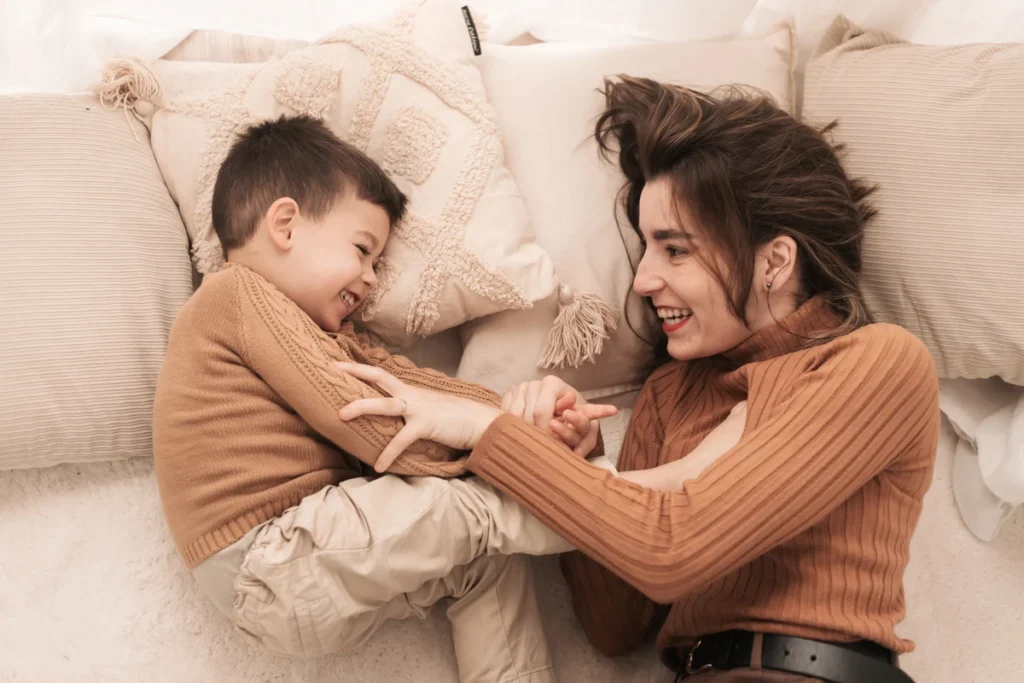 Sesión fotográfica familiar Día de la Madre - Saray Ruiz Fotografía Madre e hijo riendo juntos y abrazados durante una sesión fotográfica del Día de la Madre en estudio de Barcelona.