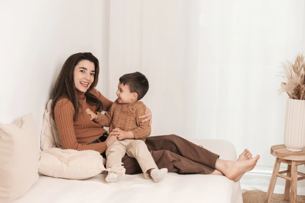 Sesión fotográfica familiar Día de la Madre - Saray Ruiz Fotografía Madre sentada abrazando a su hijo en un banco de madera en estudio profesional para reportaje del Día de la Madre en Barcelona.