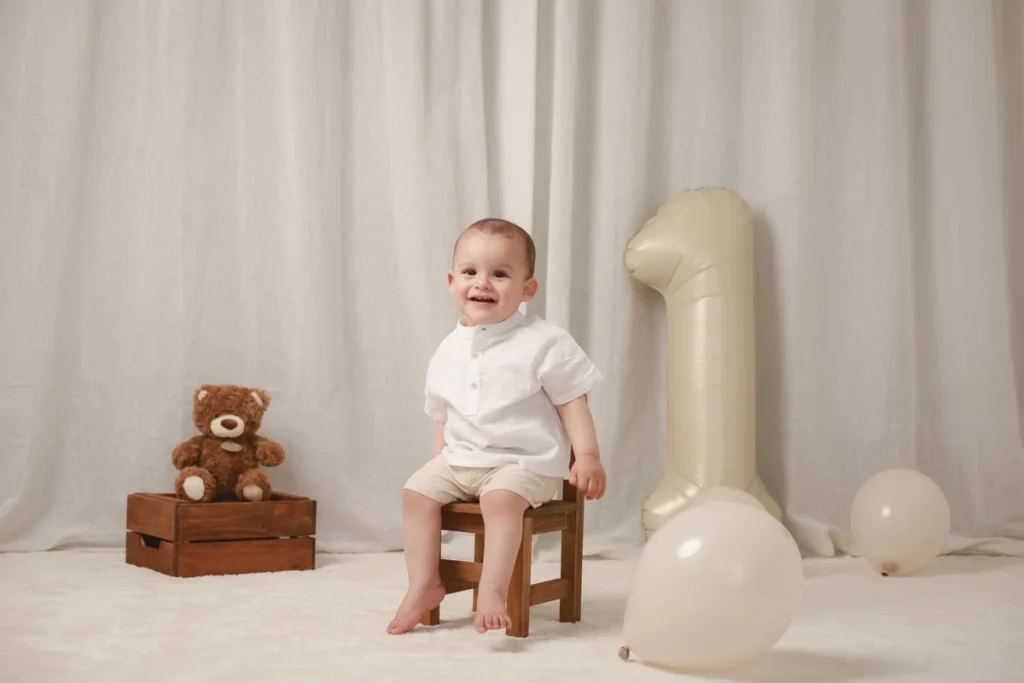 Sesión fotográfica de cumpleaños infantil en el Barcelona. Fotografía de bebé para primer cumpleaños sentado en silla de madera con decoración en tonos crema.