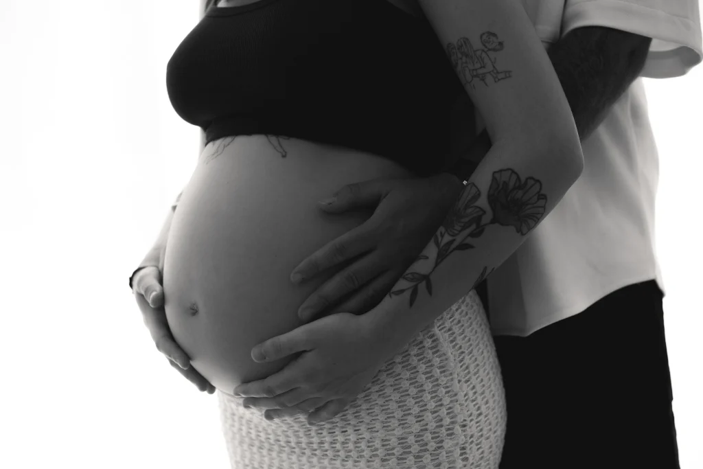 Sesión de fotos de embarazo en Barcelona - manos de la pareja abrazando la barriga en blanco y negro