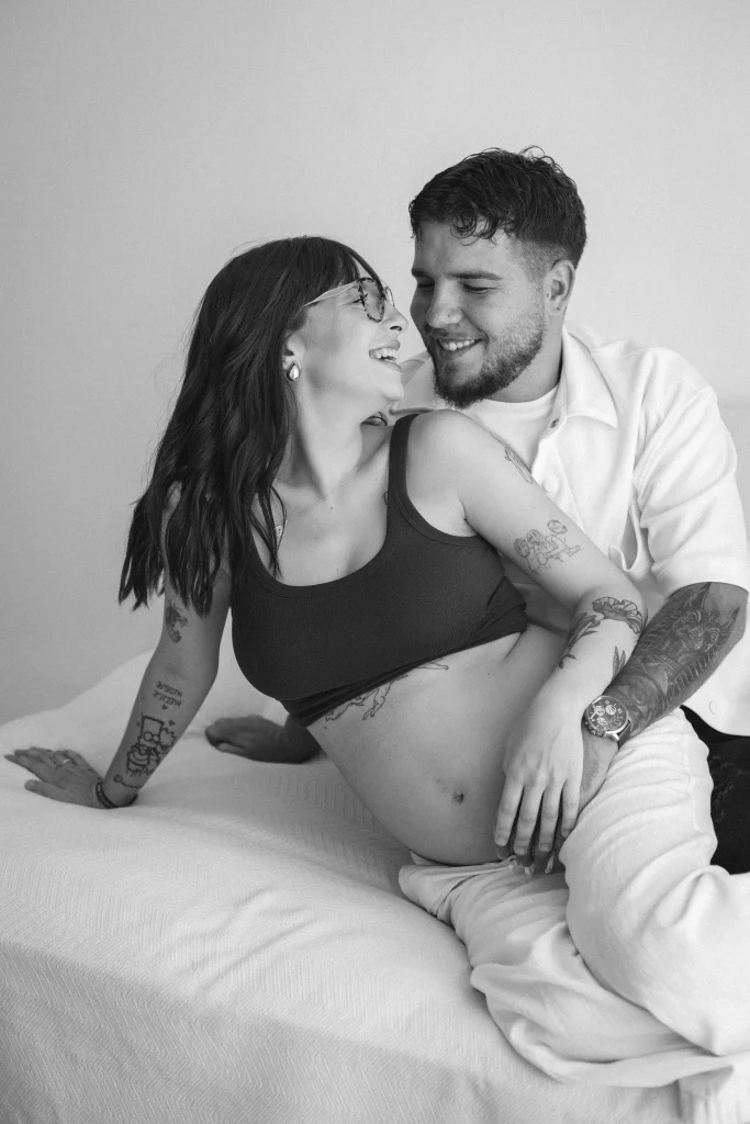 Sesión de fotos de embarazo en pareja en Barcelona, futuros padres riendo en estudio