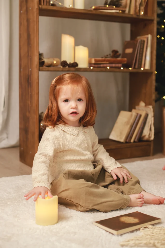 Niña sentada en el suelo junto a una estantería decorada con velas navideñas