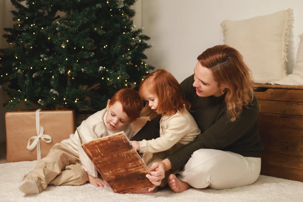 Madre leyendo un cuento con sus dos hijos sentados junto al árbol de Navidad decorado